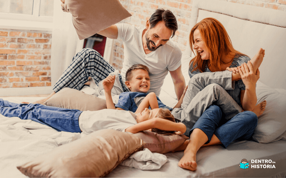 pai de familia se divertindo com seus filhos, em cima de uma cama, momento em familia bem divertido resultado de ter aprendido a como começar a economizar as finanças pessoais.