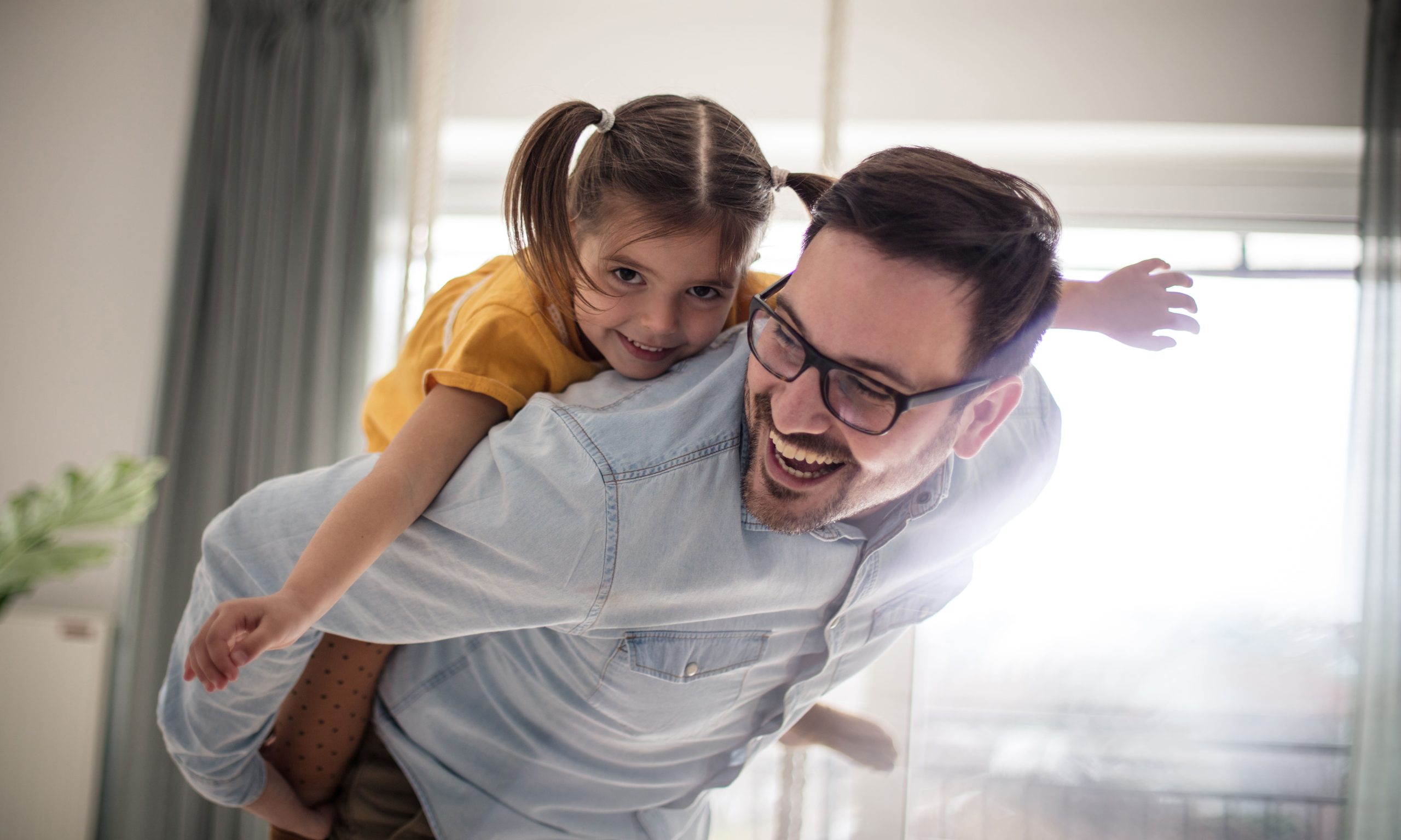 Homem adulto de óculos brincando com sua filha dando significado à liberdade financeira